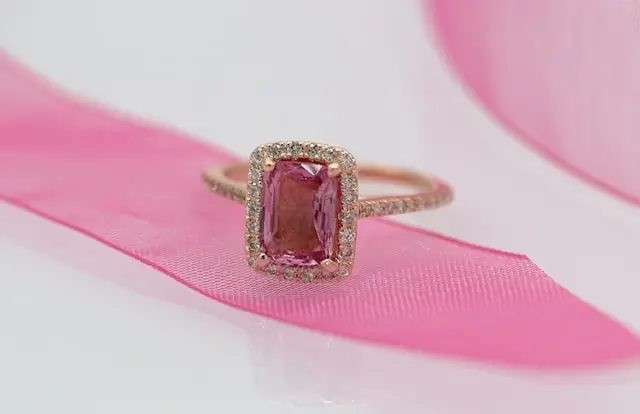 Rose gold pink sapphire ring with cushion cut center stone surrounded by diamond halo setting on pink ribbon
