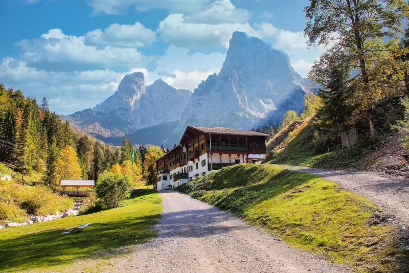 Traditional guesthouse with painted facade and wooden balconies below towering Wilder Kaiser peaks in autumn along Eagle Walk Austria