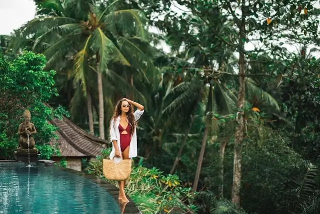 Woman enjoying infinity pool surrounded by tropical palm trees and lush jungle in Bali, Indonesia