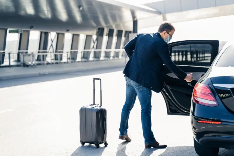 Business traveler with luggage entering luxury black sedan at airport terminal for premium chauffeur service pickup