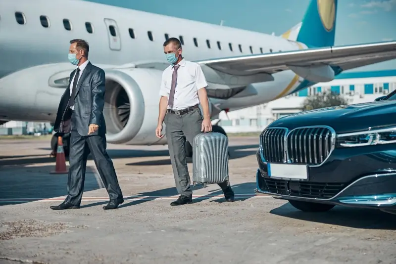 Business travelers walking from private jet to luxury car on airport tarmac for VIP transfer service