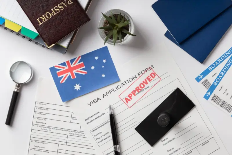 Approved visa application form with Australian flag, passport, and boarding pass on desk