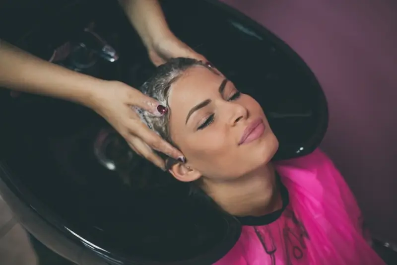 Woman receiving professional hair treatment at salon before choosing between hair botox vs keratin options