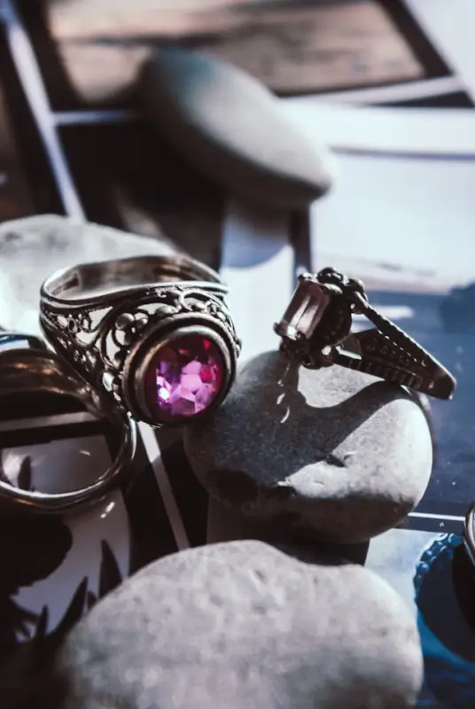 Vintage silver rings with ornate filigree settings showcasing pink sapphire center stones displayed on white pebbles