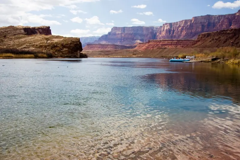 Calm river water with blue rafts docked along red canyon cliffs in desert landscape