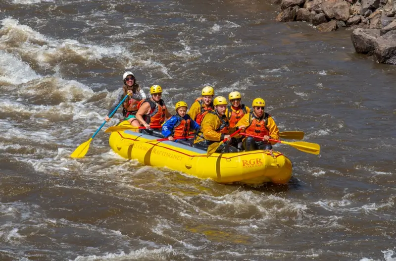 Colorado white water rafting crew in yellow raft navigating rapids with helmets and life jackets