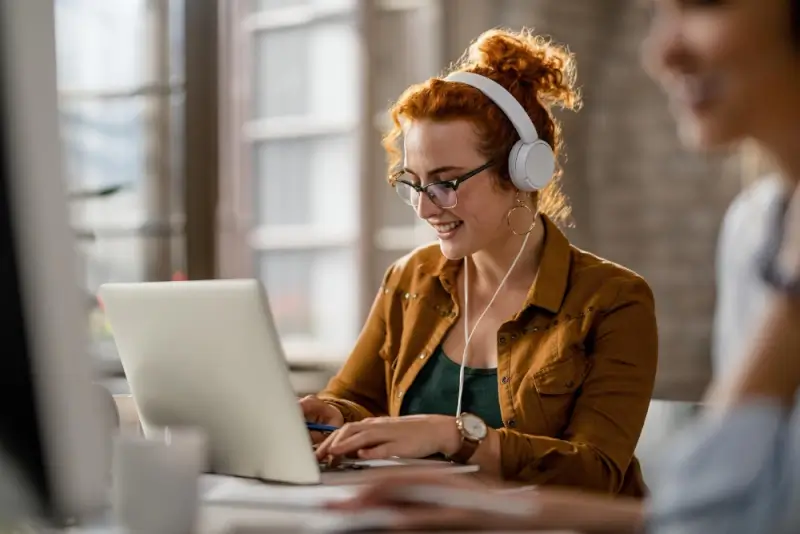 Travel content creator wearing headphones while transcribing vlog footage on laptop for multilingual audiences