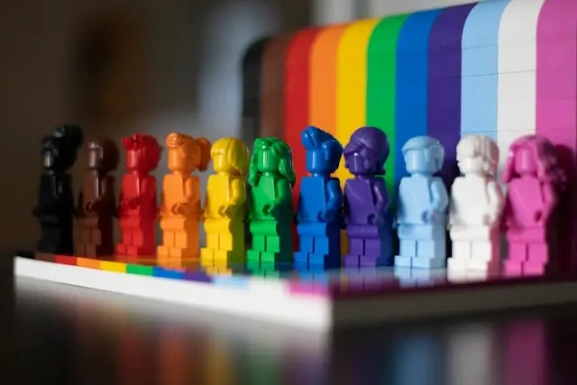 Colorful figurines arranged in a row in front of a rainbow backdrop, symbolizing diversity, inclusion, and representation within the LGBTQ community.