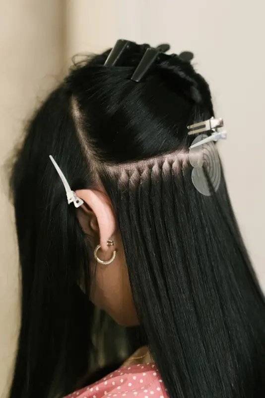 Professional stylist installing tape-in hair extensions on dark hair, illustrating how hair extensions pricing often reflects application method, precision work, and salon expertise.