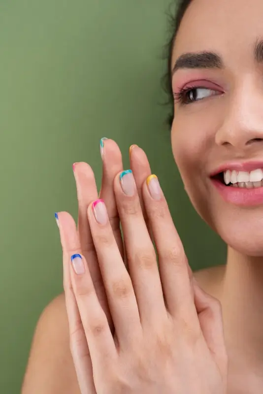Smiling woman displaying colorful French tip manicure with rainbow accents on short nails