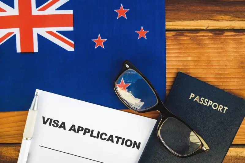 Visa application document with passport and glasses on New Zealand flag background