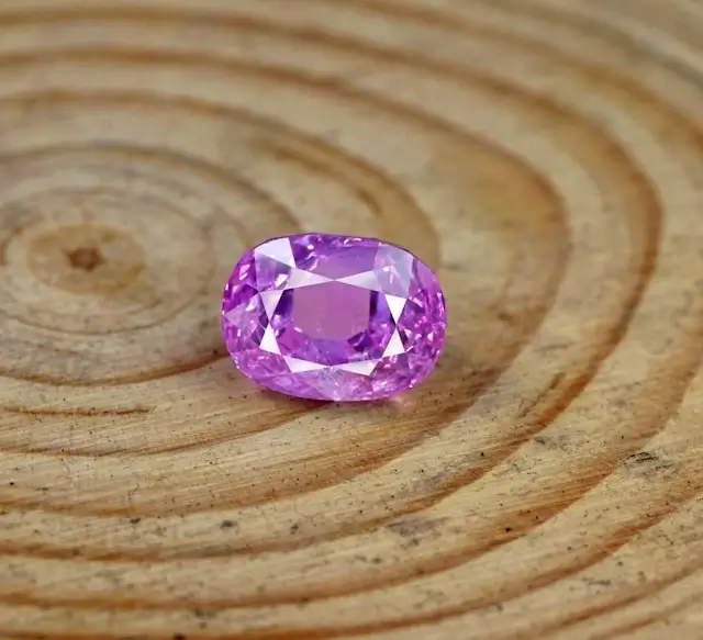 Oval cut pink sapphire gemstone with faceted surface displaying vibrant magenta color on wooden background