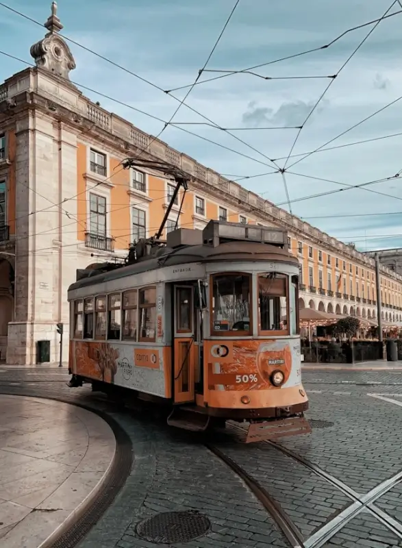 Vintage orange tram on cobblestone street in Lisbon Portugal with historic architecture and overhead electric wires