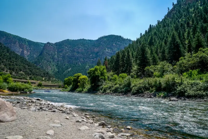 Rafting group floating down river through forested mountain canyon with rocky shoreline