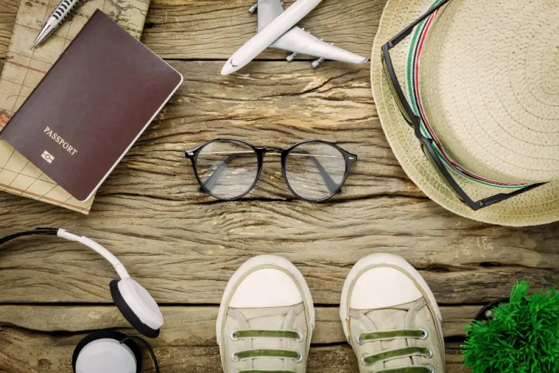 Pair of glasses on wooden table with passport, airplane model, sun hat, and travel essentials