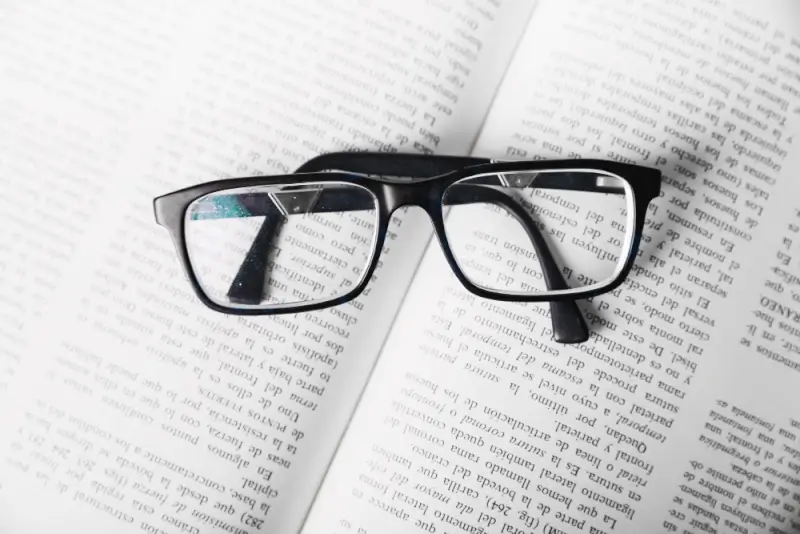 Black-framed reading glasses resting on open book pages with clear text visible through lenses