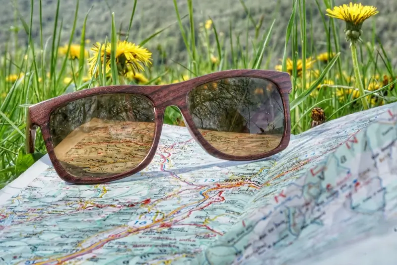 Wooden-frame sunglasses resting on colorful travel map outdoors with yellow wildflowers in background