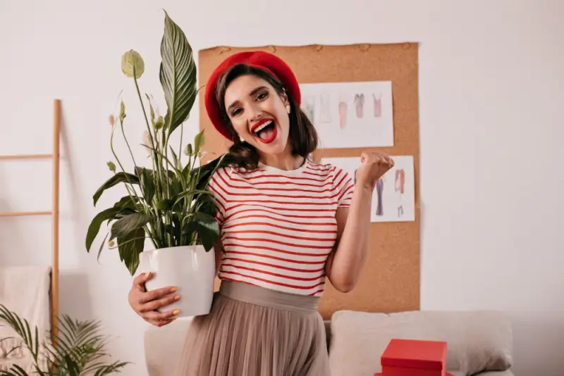 Excited woman in red beret holding potted greenery in bright modern apartment interior