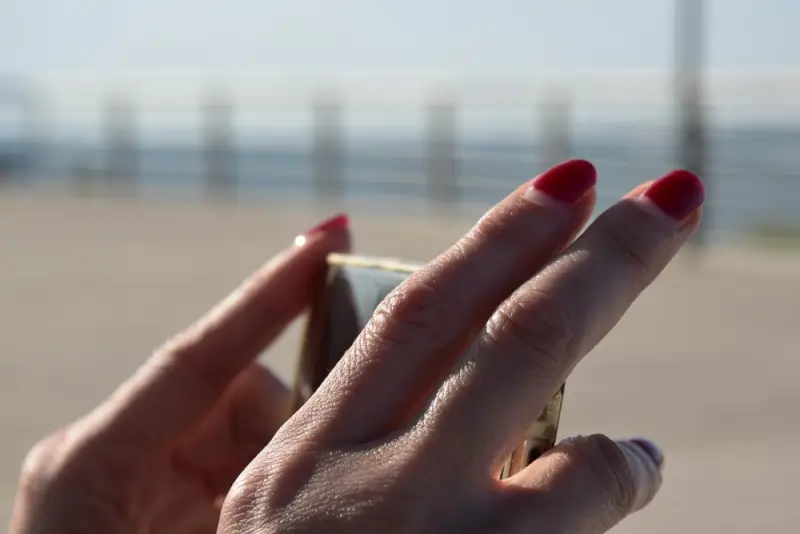 Hand with red manicure holding smartphone at the beach showing chip-free polish during travel