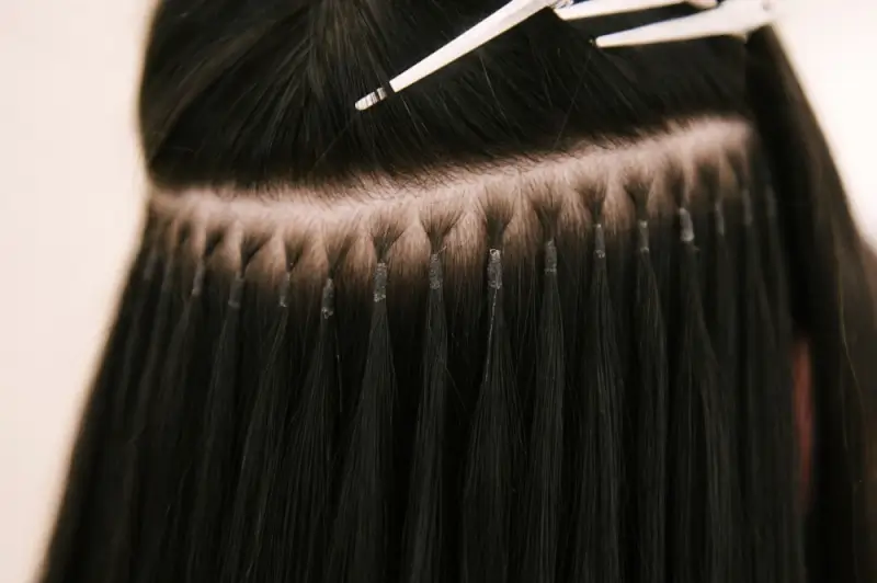 Close-up view of tape-in hair extensions attached in a neat horizontal row, showing evenly spaced adhesive tabs blended smoothly with natural dark hair.