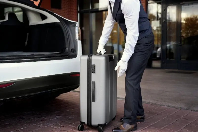 White-gloved chauffeur loading passenger luggage into trunk of premium vehicle for airport transfer service