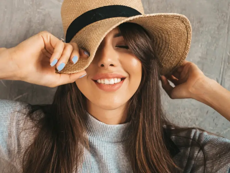 Happy traveler in straw hat showing off blue manicure that stayed intact throughout her trip