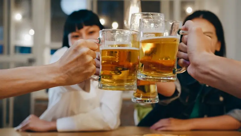 Group of friends toasting beer mugs together at restaurant emphasizing drink safety awareness while traveling