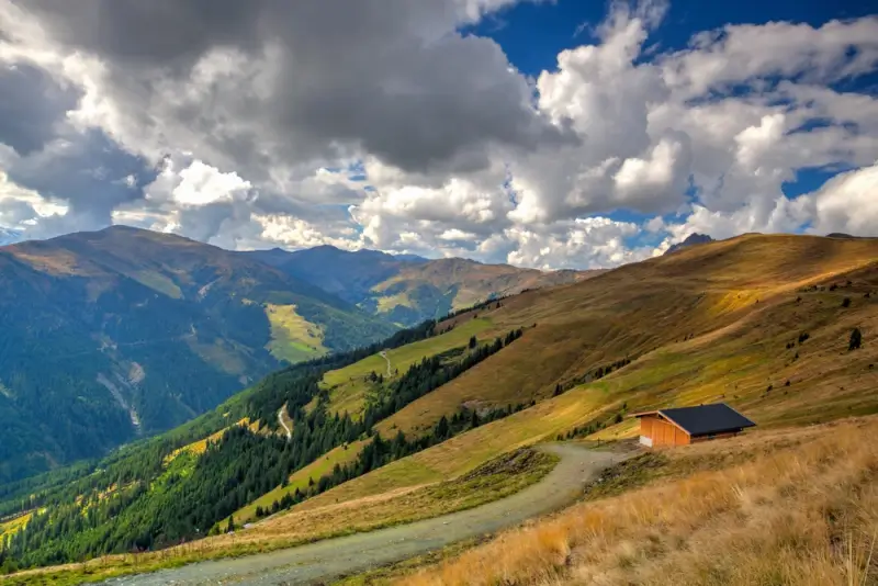 Isolated alpine barn on golden autumn hillside with dramatic cloud formations over mountain valleys in Tyrol Austria