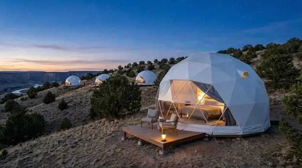 Geodesic dome tents on wooden platforms near canyon edge offering upscale camping experience at twilight
