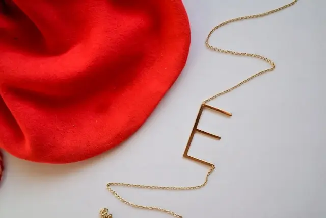 Gold initial pendant necklace featuring letter E on delicate chain with red beret accessory