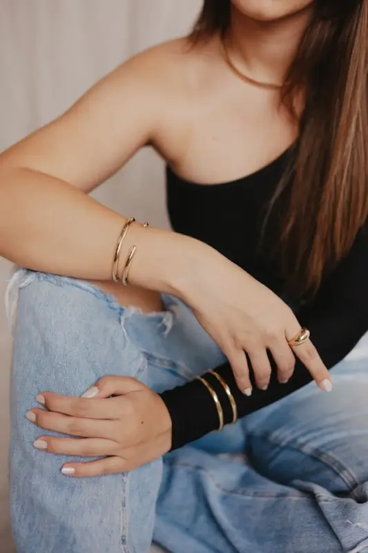 Woman wearing layered gold bangles and ring in minimalist style with casual denim outfit