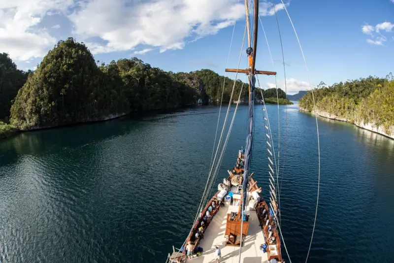 Traditional Indonesian schooner navigating through limestone karst channels in Raja Ampat, offering access to remote dive sites unreachable from land-based resorts