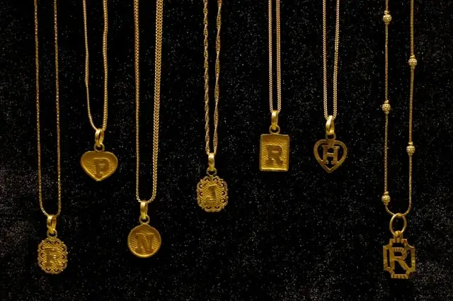 Collection of gold initial pendants displaying various letter designs and shapes on black velvet background