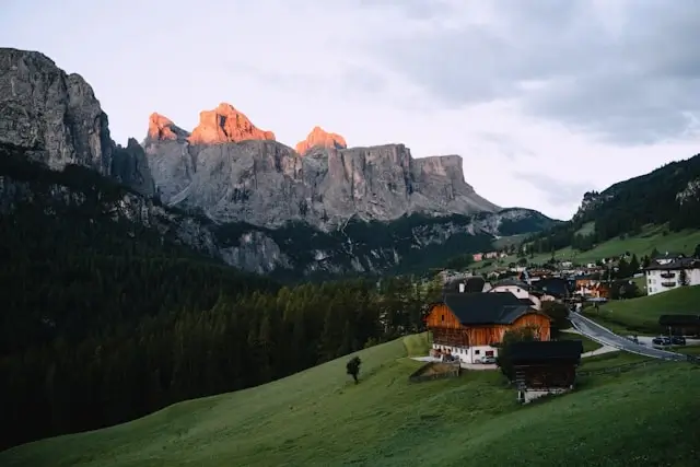 Mountain village with wooden chalets on hillside below limestone cliffs glowing orange during sunset alpenglow