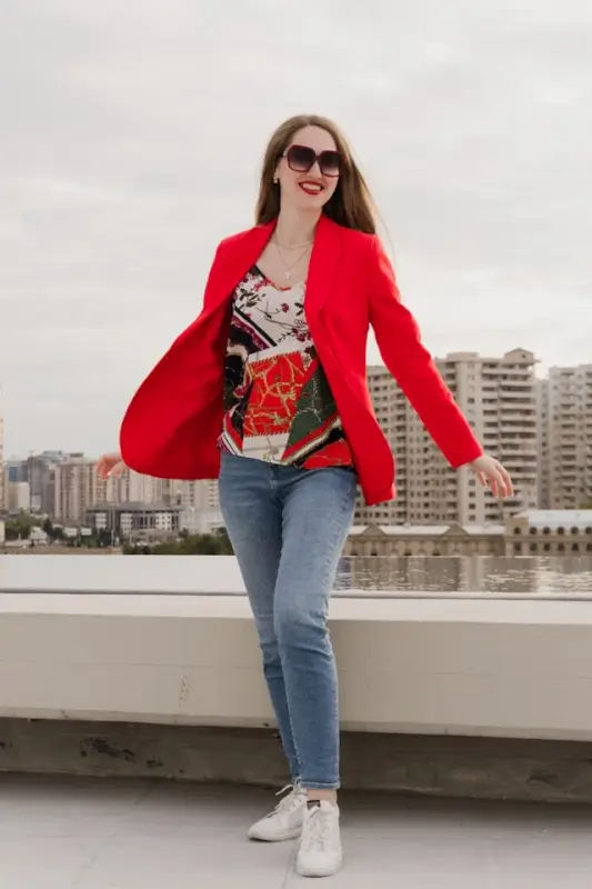Woman in red blazer layered over patterned blouse with jeans and white sneakers for casual to polished look