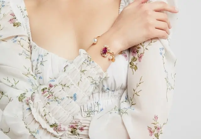 Woman wearing delicate charm bracelet with floral print blouse showing minimal jewelry for daytime office wear