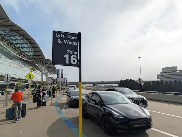 Designated rideshare pickup zone at airport terminal with parked vehicles waiting for passengers