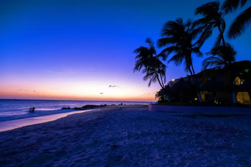 Sunset view at Divi Beach with palm trees and beachfront bars lighting up for evening