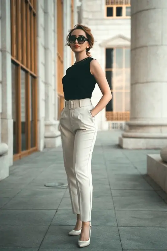 Woman in black sleeveless top with beige belted trousers and white heels showing polished city style