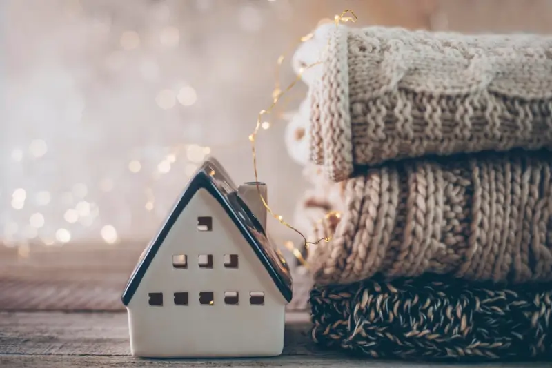 Cozy home decor with knitted blankets, fairy lights, and decorative house creating warm atmosphere