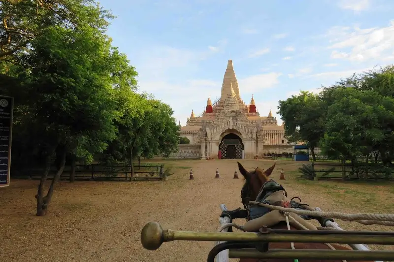 Horse cart approaching Ananda Temple through tree-lined grounds in Bagan, Myanmar