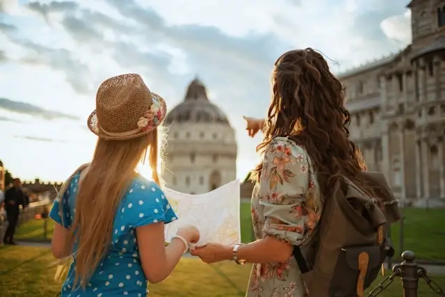 Two women travelers reading a map in Pisa, Italy, with the Baptistery of St. John in the background