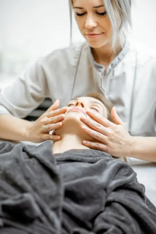 Beauty school student practicing manual facial massage techniques on client during hands-on training