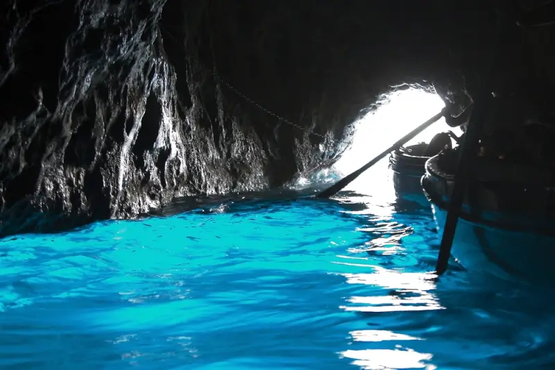 Inside the Blue Grotto sea cave with glowing electric blue water and rowboat guide navigating through the entrance