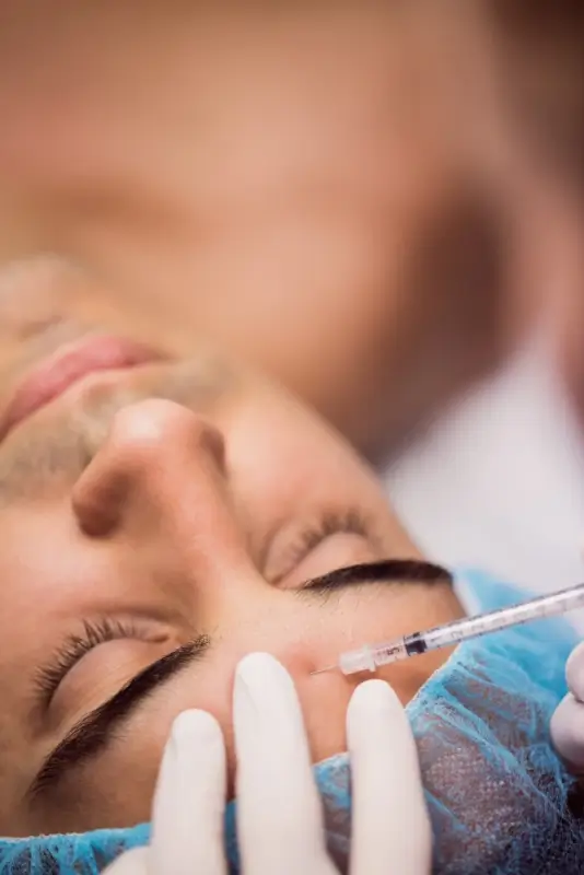 A gloved doctor administering a botox injection near a patient's eye area during a facial treatment