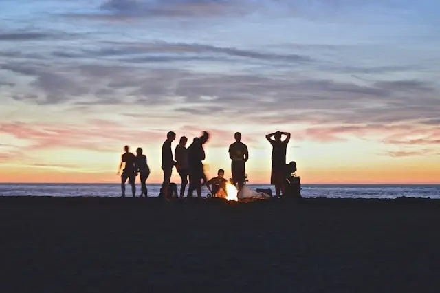 Group of friends enjoying buddymoon beach bonfire at sunset before wedding day