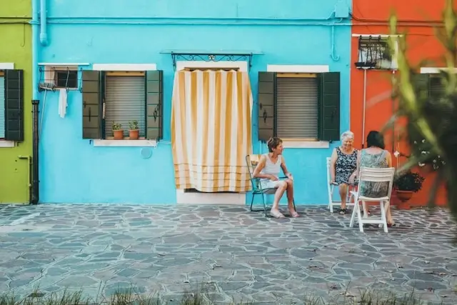 Two local women having a conversation outside colorful houses on the island of Burano, Italy