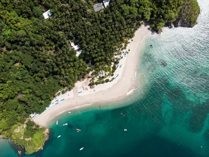 Aerial view of secluded beachfront resort nestled in tropical rainforest along turquoise Costa Rican coast