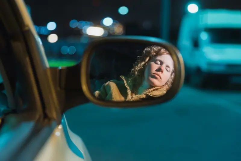 Woman appearing drowsy in car side mirror reflecting dangers of impaired driving at night