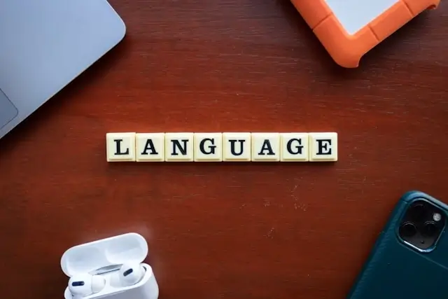 Scrabble tiles spelling the word LANGUAGE on a wooden desk surrounded by everyday tech gadgets